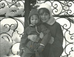 Sean Hepburn Ferrer sitting in Audrey Hepburn's lap in the snow against a fence as a child.