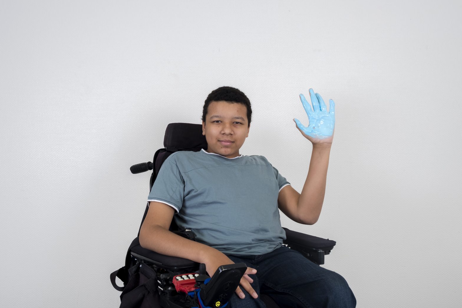 An image of Lubin with his palm painted blue sitting in a mobility chair.