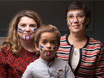 The image shows three people with their faces painted in blue and pink.