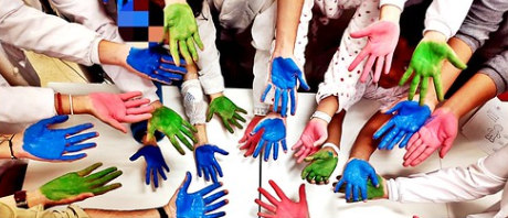 An image of people holding out their palms painted in blue, green and pink.